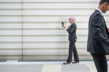 Muslim Business People on their Smartphone while on a coffee break, walking towards each other. Shallow depth of field.