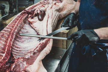 Midsection of man wearing apron cutting pig carcass in butcher shop