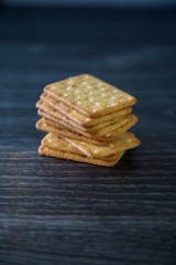 Tower of crackers waiting to be eaten with cheese and crackers as part of a cheeseboard for dessert. Sitting on a wood grain kitchen bench, dark background. Isolated. Bought from supermarket.