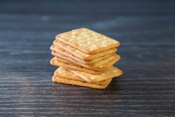 Tower of crackers waiting to be eaten with cheese and crackers as part of a cheeseboard for dessert. Sitting on a wood grain kitchen bench, dark background. Isolated. Bought from supermarket.