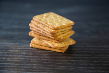 Tower of crackers waiting to be eaten with cheese and crackers as part of a cheeseboard for dessert. Sitting on a wood grain kitchen bench, dark background. Isolated. Bought from supermarket.