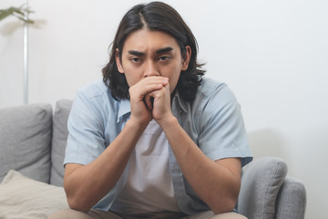 Depressed asian man sitting on the sofa regret about his fault.