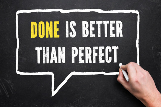 hand is drawing speech bubble with text "done is better than perfect" on chalkboard