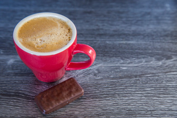Homemade espresso flat white in bright red cup on dark wood background. Perfect with a chocolate biscuit. Feelings of warmth, luxury, reward. Contrast with red, wood and rich chocolate. Tantalising.