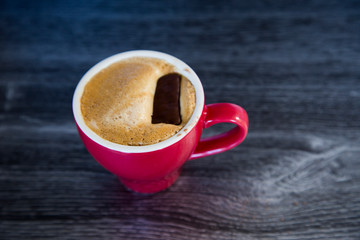 Homemade espresso flat white in bright red cup on dark wood background. Perfect with a chocolate biscuit. Feelings of warmth, luxury, reward. Contrast with red, wood and rich chocolate. Tantalising.