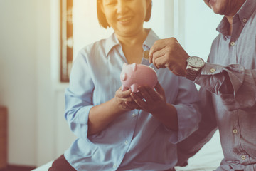 Senior asian couple hands putting coin to piggy bank for retirement together,Saving money concept