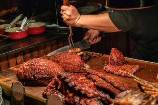 The Chef Cutting Baked Ham And Sausage In Restaurant