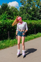 Portrait of an emotional girl in a pink cap visor and protective gloves for rollerblades and skateboarding riding on rollerblades on the road.