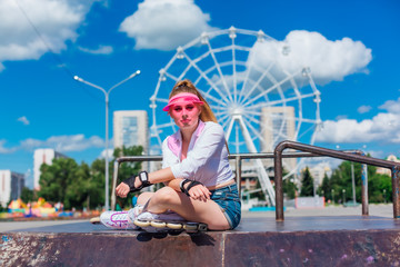 Portrait of an emotional girl in a pink cap visor wearing protective gloves and rollerblades...