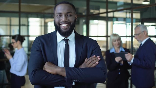 Smiling african businessman in suit folding arms, office work, corporate success
