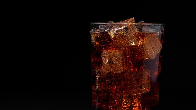 Pouring coca cola into the glass. Closeup on black background. Slow motion shot
