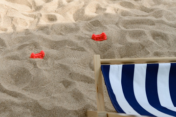 sun lounger and plastic toys in the shade on sand