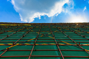 outside of an unfiinshed building with protection scaffolding and netting under blue sky