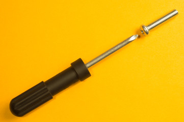 Screws and screwdriver on a yellow background