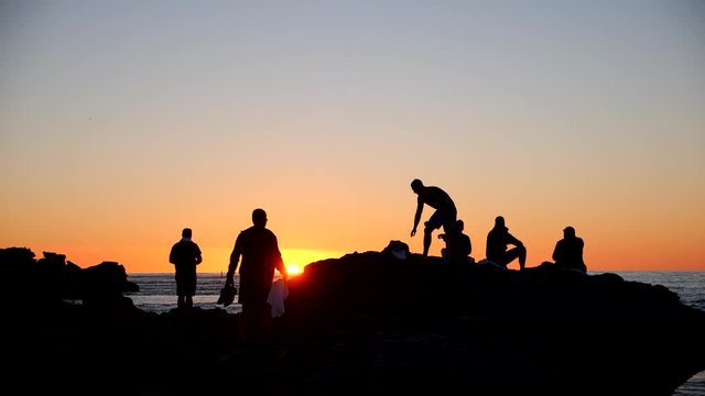 People watching sunset from rocks on beach silhouette