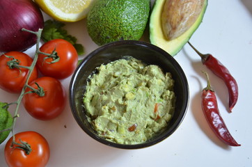 A delicious Bowl of Guacamole next to fresh ingredients on a table with tortilla chips and salsa. sandwich with guacamole, red hot pepper, lime, lemon, avocado