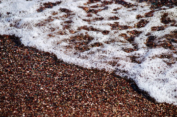 sea wave with white foam on the beach with small pebbels and sand