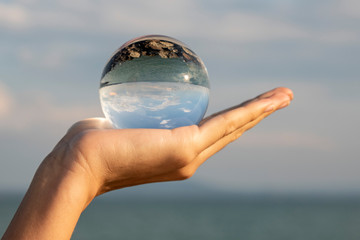Lens-ball on the female palm. It reflects the sky, clouds and the sea.