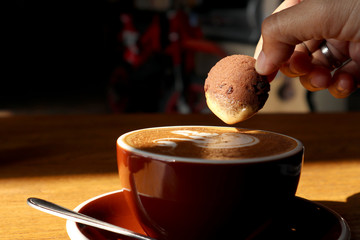 female dipping one chocolate cookie over a coffee latte