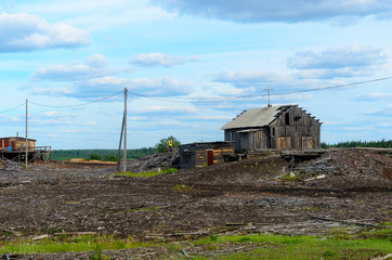 Fototapeta na wymiar An old abandoned sawmill stands on the Bank of the Northern river and in the forest with littered boards and old buildings in Yakutia in the village of Suntar.