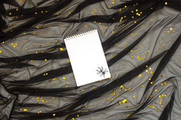 Abstract background with  black tulle strewn with golden confetti, notepad and spider, concept for Halloween.