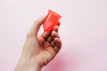 Woman's hand holding menstrual cup over pink background.