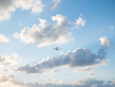 Flying plane in the sky with clouds at sunset as a background