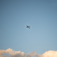 Flying plane in the sky with clouds at sunset as a background