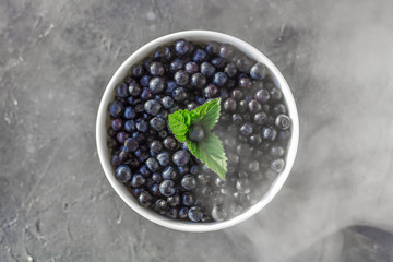Fresh organic blueberries in a bowl on dark background in smoky effect close up.