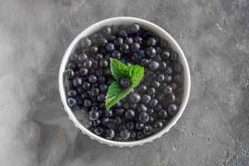 Fresh organic blueberries in a bowl on dark background in smoky effect close up.
