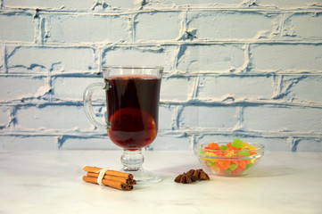 Glass cup with mulled wine and lemon with a bunch of cinnamon sticks, anise stars and a bowl of...
