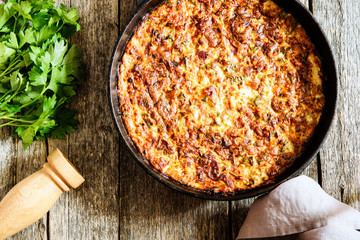 Zucchini Casserole with Bacon and Cheese in cast iron pan and parsley bunch and pepper mill on...