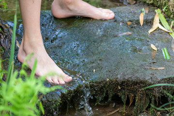 Kind kühlt seine nackten Füße in kaltem frischem Quellwasser eines kleinen Baches im Sommer und...