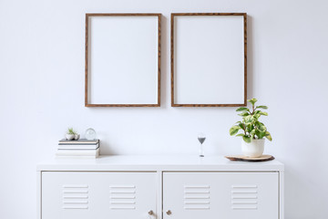 Minimalistic home decor of interior with two brown wooden mock up photo frames above the white shelf with books, beautiful plant in stylish pot and home accessories. White wall. Concept of mockup.