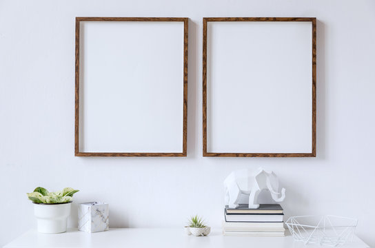 Stylish white home decor of interior with two brown wooden mock up photo frames on the white shelf with books, beautiful plant in stylish pot, elephant figure and home accessories. 