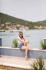 Fashion model in blue shorts and white shirt posing for photographer in beautiful inflow. Stylish woman in sunglasses