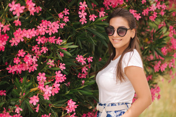 Gorgeous woman in sunglasses stand in beautiful flowers. Portrait of happy smiled young woman