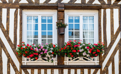 Fototapeta na wymiar Two windows in a half-timbered house decorated with the flowers outside. Normandy, France.