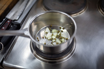 Green capers and sliced white onion cocking in the steel pot
