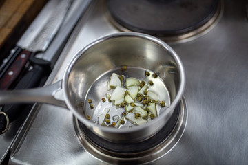 Green capers and sliced white onion cocking in the steel pot