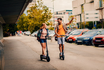 Young couple on vacation having fun driving electric scooter through the city.	