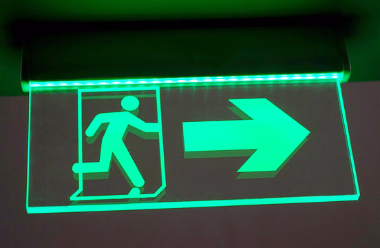 Illuminated fire or emergency exit sign,hung on wall,in a public place       