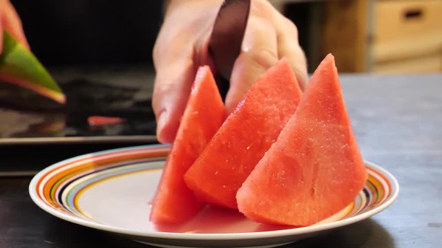 MAN CUTTING A JUICY WATER MALON ON A COLOURFUL PLATE