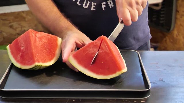 MAN CUTTING A JUICY WATER MALON ON A COLOURFUL PLATE
