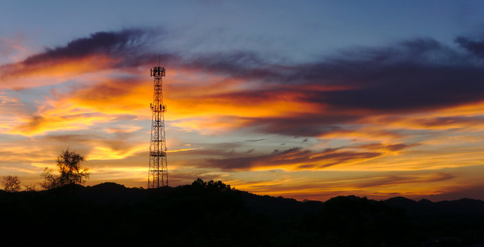 Panorama shot of Tall mobile cell phone tower on the high hill sending signal to connect people around the world in the evening when sunset with orange red sky and clouds with copy space on the right.