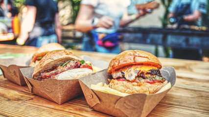  Street food festival background. Delicious burgers and French fry closeup served on a wooden table. Open kitсhen and team of chefs shown with a low-depth of field.