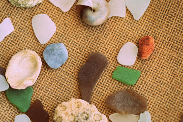 Shells, sea glasses and stones on a jute background close-up brown color toned. Vacation concept