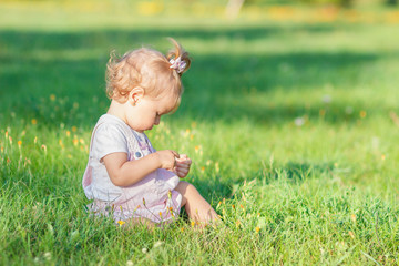 Fototapeta premium Cute little girl sits on the green grass, outdoors, summer time, blurred background