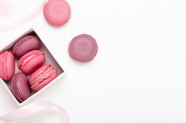Box with colorful macaroons on a white background with ribbons. Sweet treat, pastries, high-calorie food. Copy space, top view, flat lay