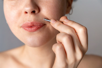 A young woman plucks her hair over her upper lip with tweezers. The concept of getting rid of unwanted facial hair. Close up